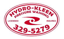 A pressure washing service cleaning a concrete driveway, water spray visible, surrounded by grass and a residential home.