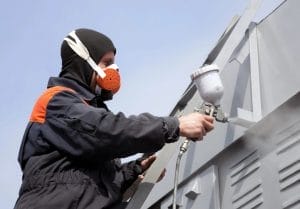 Man spray painting a house with white paint