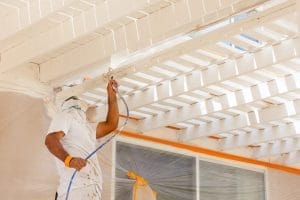 Man spray painting a wooden ceiling structure with white paint